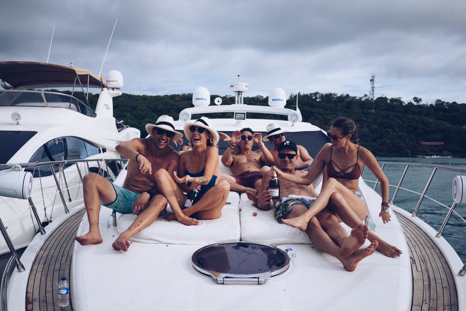 Small group of friends relaxing and laughing on sunbed cushions on the bow of a luxury motor yacht.