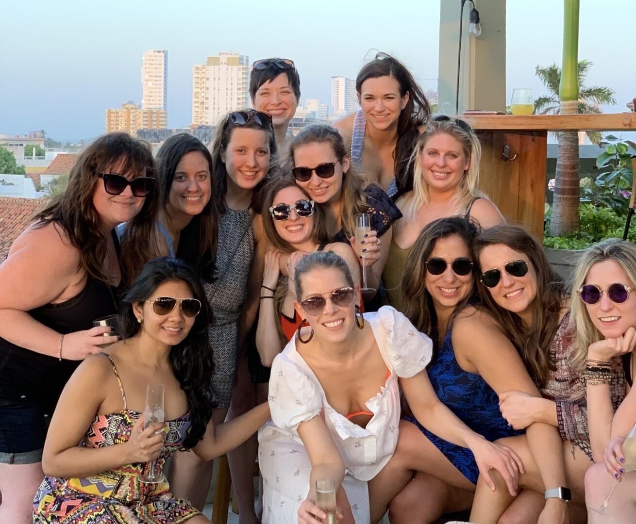arge group of women in stylish resort wear and sunhats cheering and toasting tropical cocktails on a private beach setup in Cartagena.