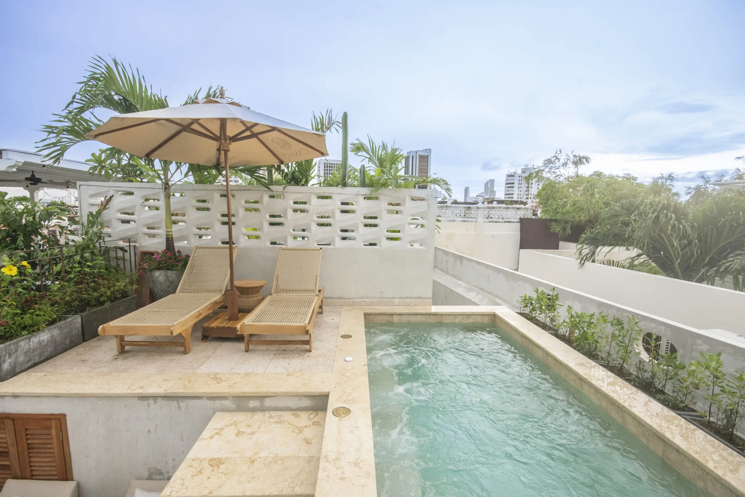 Luxury rooftop swimming pool with wooden daybeds and a white sun umbrella at Casa Carbonera Cartagena.