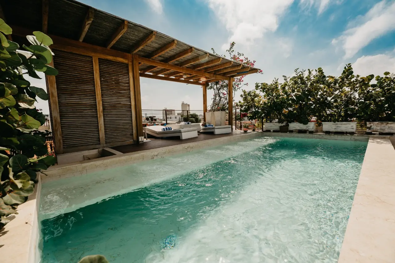Elevated rooftop swimming pool surrounded by modern white daybeds and wooden pergolas at Villa Chirimoya Cartagena.