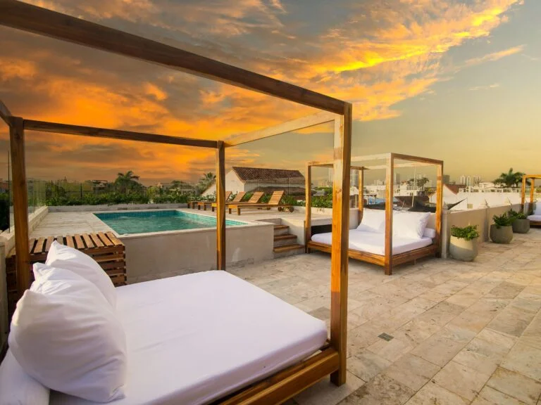 Sunset view of a luxury villa rooftop terrace with plush canopy daybeds and swimming pool at Two Travel Home.
