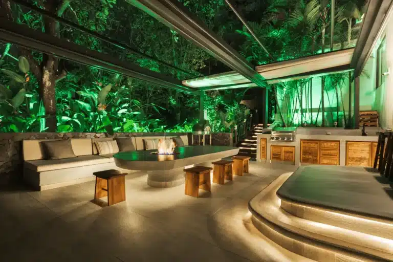 Modern illuminated outdoor lounge with central fire pit table and tropical greenery surrounding a private villa at Two Travel Home.