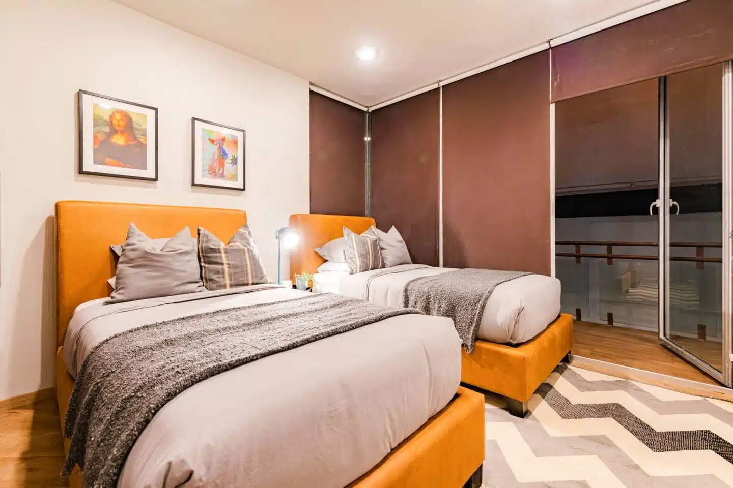 Elegant bedroom with two beds featuring yellow-orange headboards next to a glass door at Potosi Mexico City.