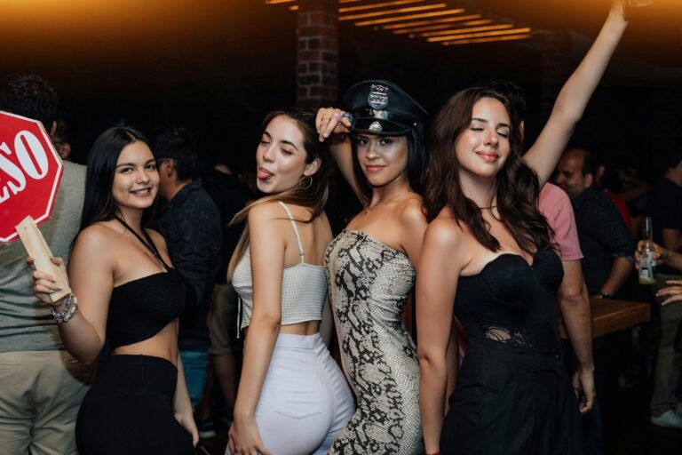 Four stylish women dancing and posing inside a lively nightclub during a party at Two Travel Home.