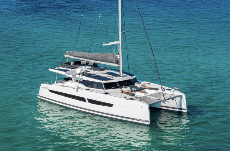 White luxury catamaran sailing on turquoise Caribbean ocean waters with guests sunbathing at Two Travel Home.