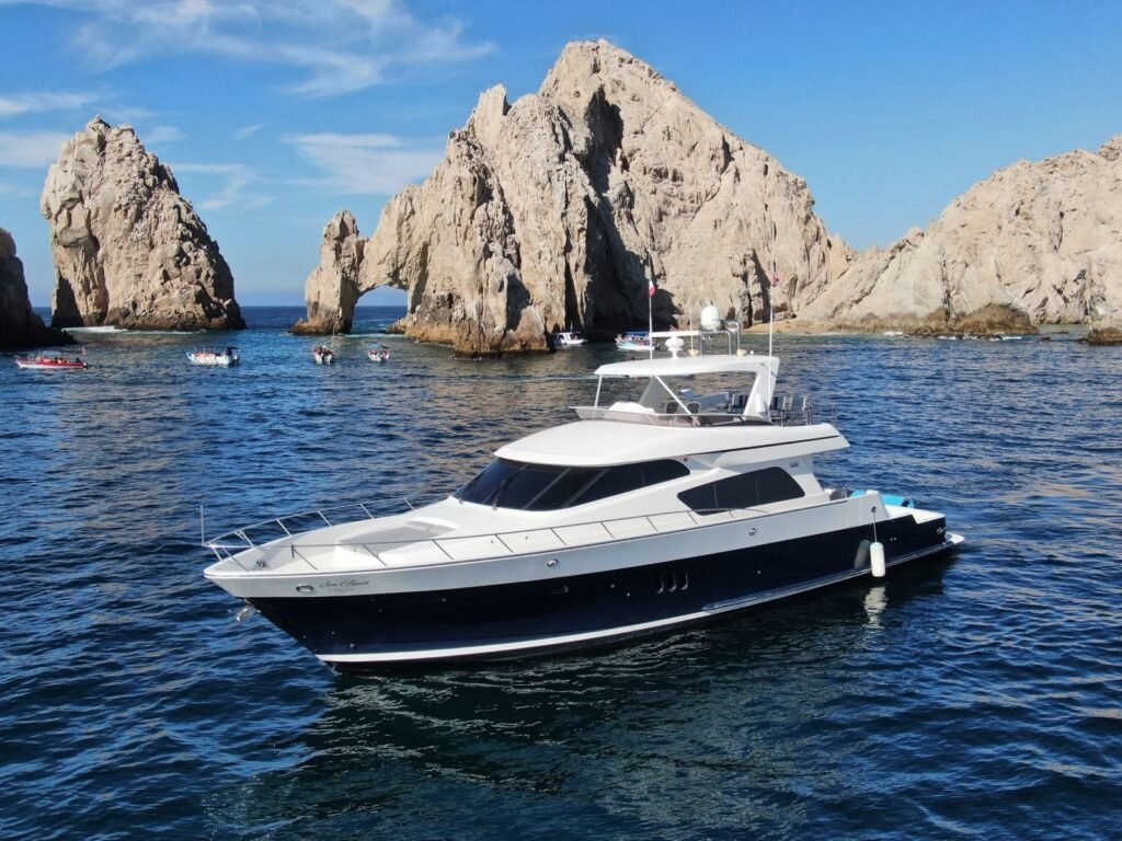 White and navy blue luxury yacht anchored in clear turquoise water with guests relaxing on a floating blue mat at Mckinna Luxury Cabo San Lucas.