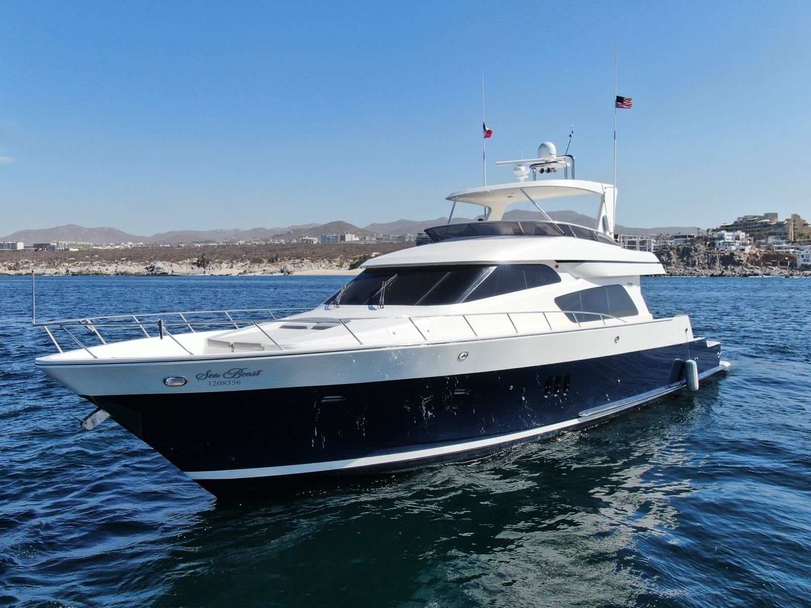 White and navy blue luxury yacht anchored in clear turquoise water with guests relaxing on a floating blue mat at Mckinna Luxury Cabo San Lucas.