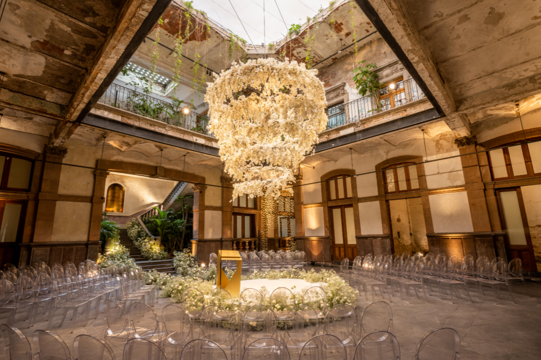 Grand wedding ceremony hall with a massive floral chandelier and ghost chairs at General Prim Mexico City.