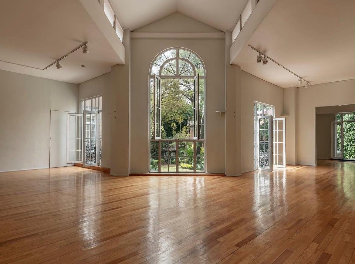 Large empty gallery room with gleaming wood floors and a towering arched window at Casa Lamm Mexico City.