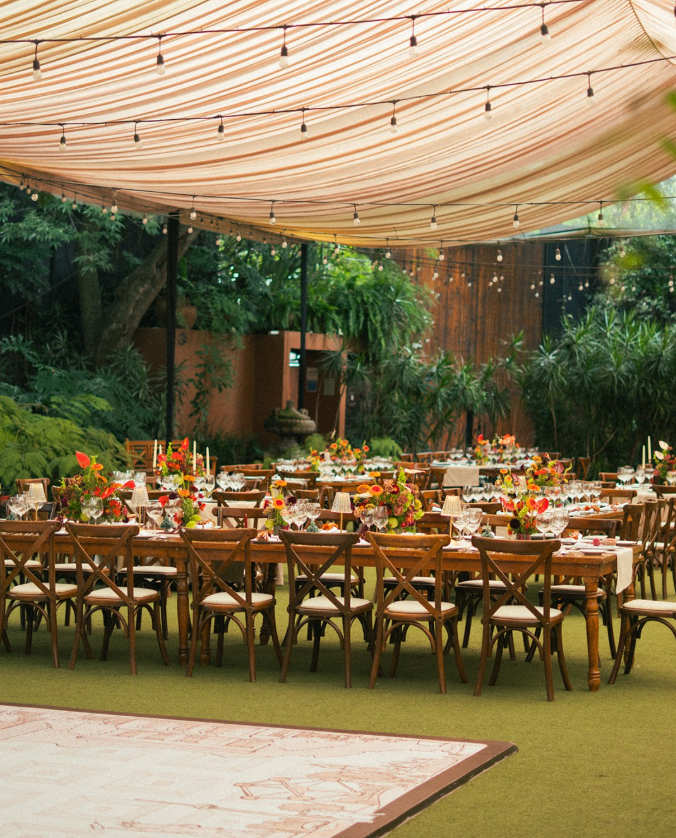 Long wooden wedding dining tables with vibrant warm-toned flower centerpieces on a lawn at Casa Xipe Mexico City.