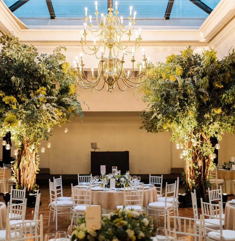 Indoor wedding banquet hall decorated with large green trees and a crystal chandelier at Hacienda Los Morales Mexico City.