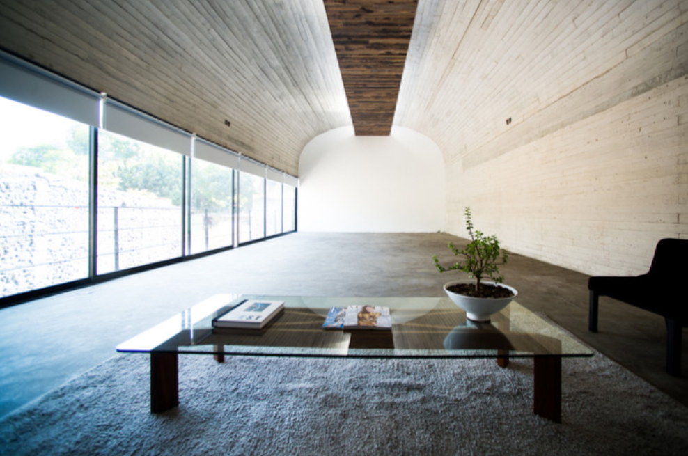 Bright empty modern pavilion room with long glass windows and a curved concrete ceiling at Rebollar Mexico City.