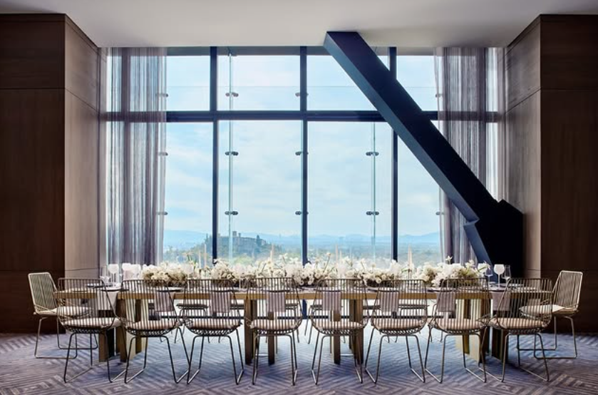 Grand empty banquet hall with long glass tables and white floral centerpieces facing a city backdrop at The Ritz-Carlton Mexico City.