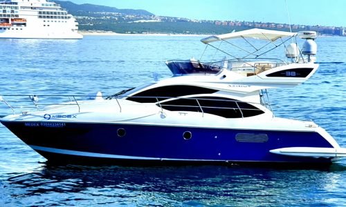 The stylish Azimut Blue motor yacht showcasing its signature navy blue hull, elevated flybridge helm station, and sleek Italian silhouette while anchored near the scenic Baja coastline.