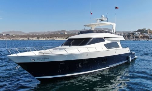 White and navy blue luxury yacht anchored in clear turquoise water with guests relaxing on a floating blue mat at Mckinna Luxury Cabo San Lucas.
