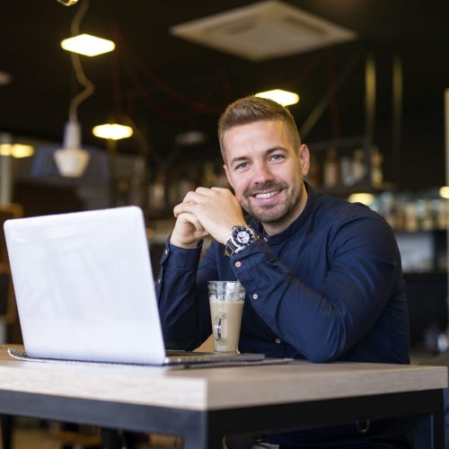 Portrait of smiling man sitting in a cafe bar with his laptop computer.